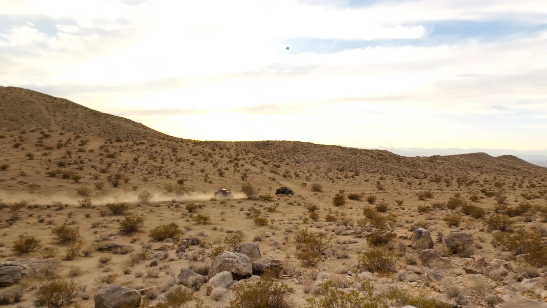 The athlete's view inside the headset of two off-road vehicles kicking up dust across desert scrubland in 180-degree Apple Immersive Video, with a small green session indicator overhead
